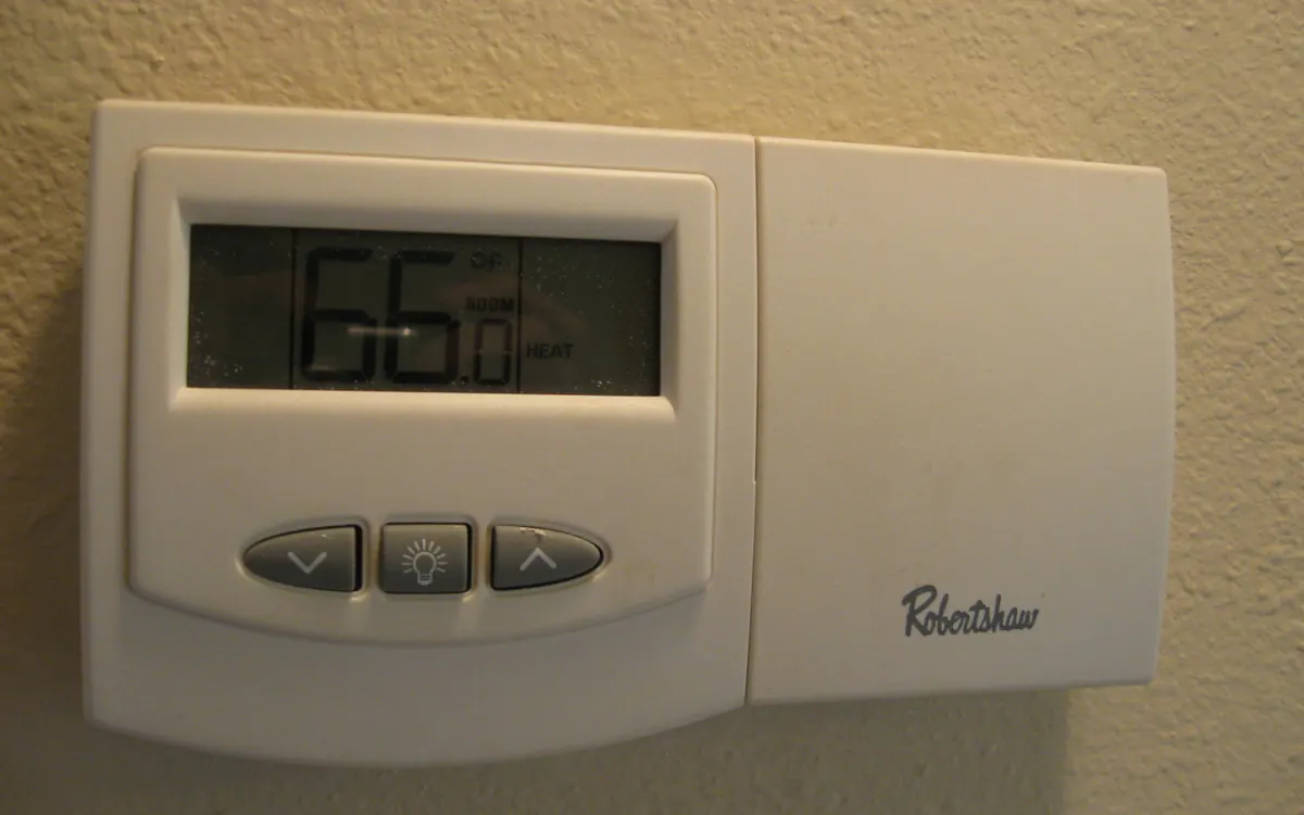 A wall thermostat set to heat showing a room temperature of 66 degrees