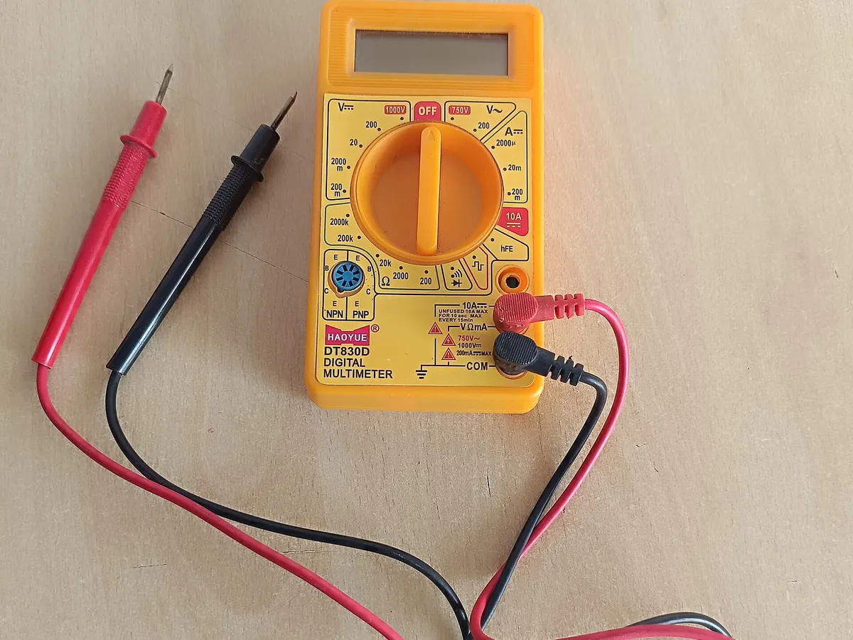 A yellow digital multimeter with red and black test leads on a wooden table